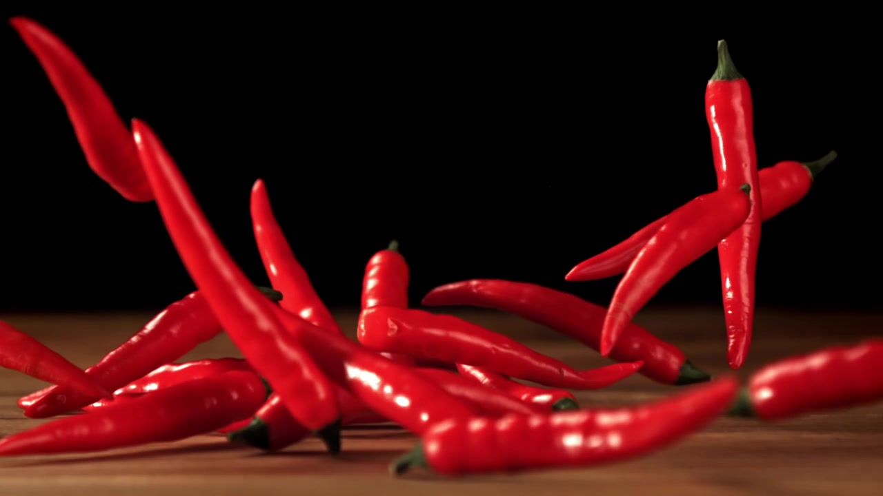 Red Chili Peppers Falling onto a Wooden Table in Slow Motion