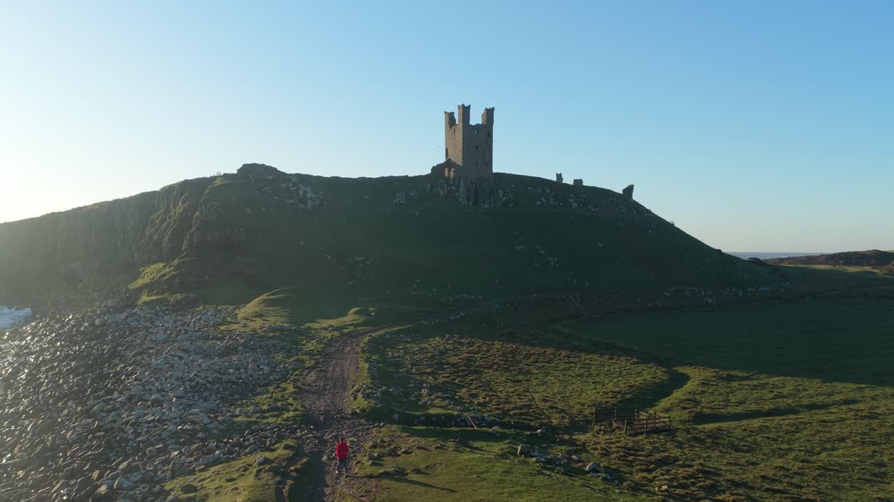 Ruinerne af Dunstanburgh Castle på Northumberlands kyst under solopgang