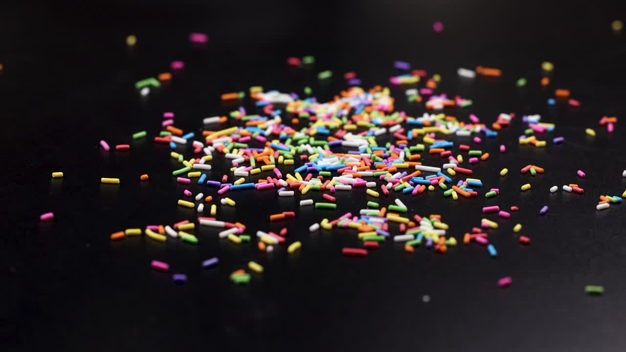 Vibrant sprinkles cascade onto a dark background