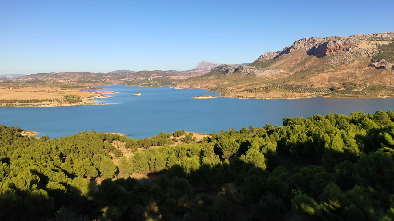 drone volando a través de la brecha de rocas y pinos para revelar una vista impresionante del lago y el terreno montañoso en un día claro y soleado