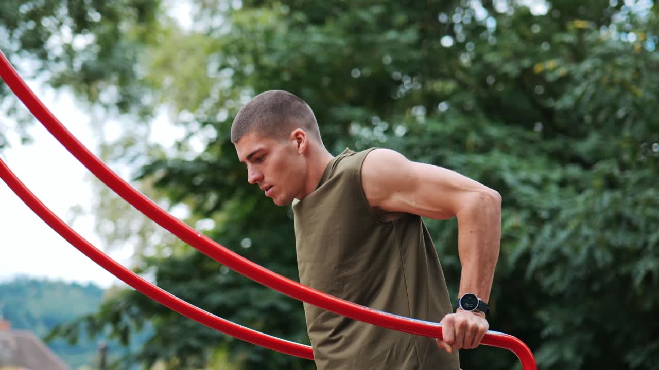 un hombre entrena flexiones en un dispositivo de entrenamiento en un parque público. sesión de entrenamiento de monitoreo con reloj inteligente.