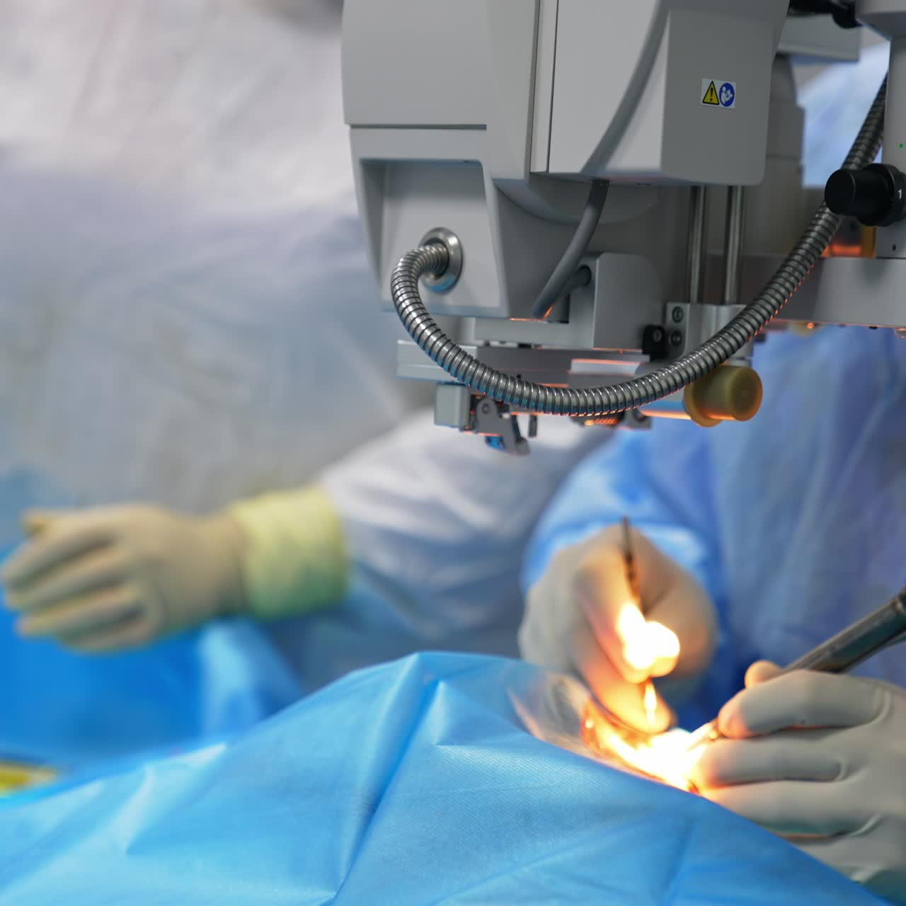 Dispositivo tecnológico que ilumina el ojo intervenido. El cirujano utiliza instrumentos para realizar la operación. Fondo difuminado.