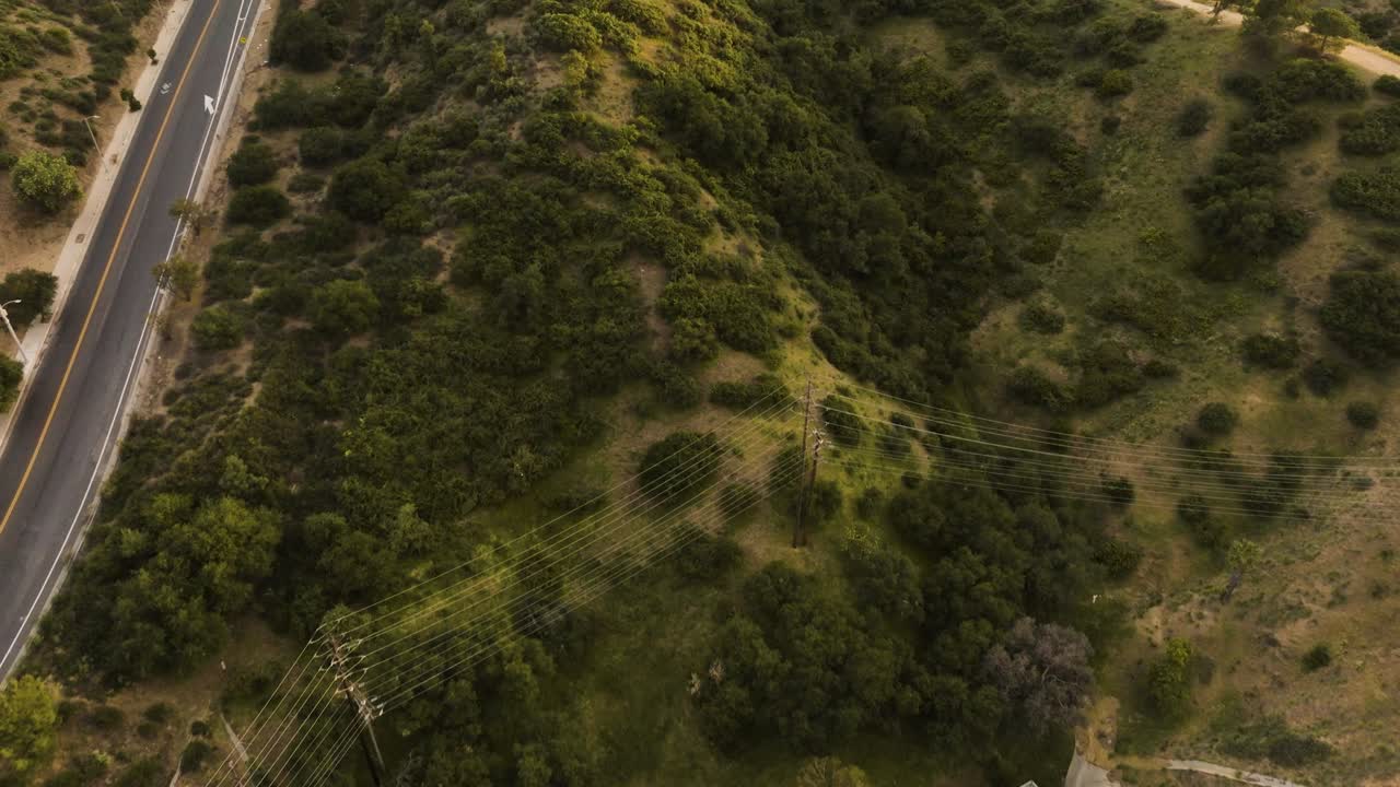 drone up a grassy hill in Los Angeles with power lines and a road