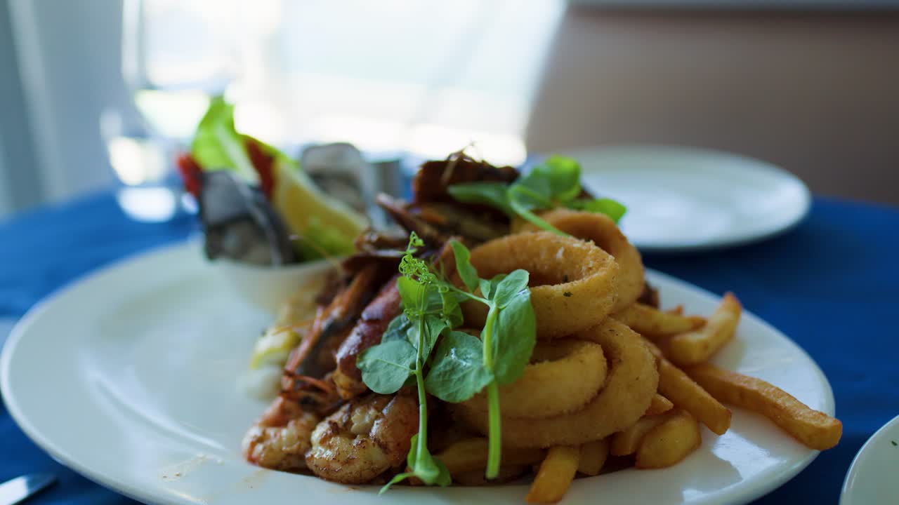 Hand uses fork to pick up calamari ring from seafood plate in bright restaurant