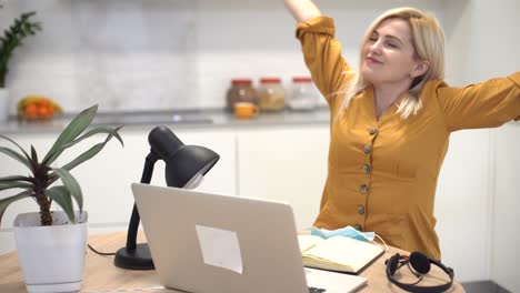 woman in protective mask works remotely on laptop at home in the kitchen, woman takes off mask