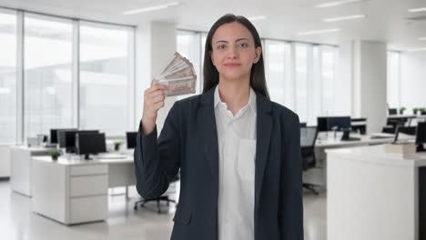 mujer de negocios india usando el dinero como ventilador con una sonrisa astuta