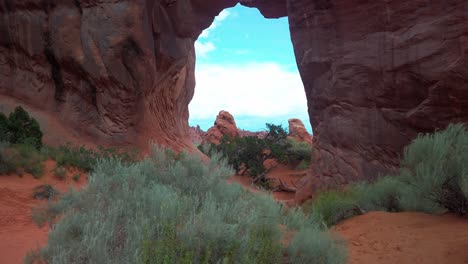 Tilting-up-shot-from-desert-bush-to-Pine-Tree-Arch-at-Arches-National-Park,-Utah