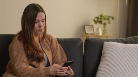 Woman-Sitting-On-Sofa-At-Home-Using-Mobile-Phone-To-Check-Social-Media-Message-And-Scrolling-Online-8