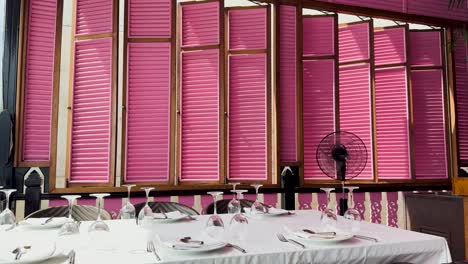 a beautifully arranged dining table with pink shutters in a bright, sunlit restaurant setting