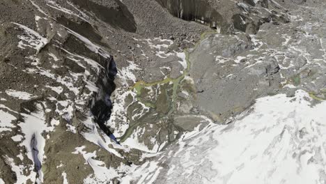 aerial view of morteratsch glacier - braided meltwater flowing through rocky terrain in bernina range, switzerland. orbiting drone shot