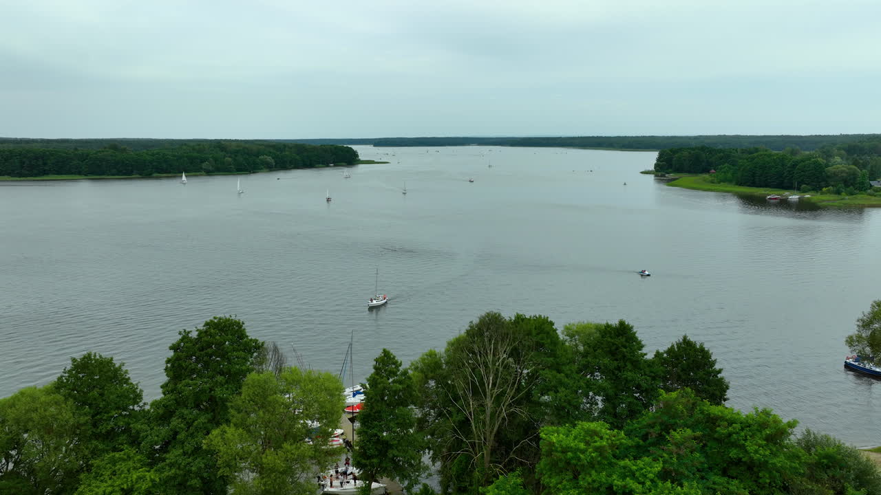 Expansive aerial view of Jeziorak lake, with sailboats drifting on calm waters, small islands, and a distant horizon, offering a perfect setting for nature and outdoor adventure