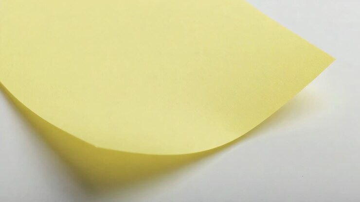Showing yellow sticky note uncurling on white surface, adhesive releasing and shadow shrinking