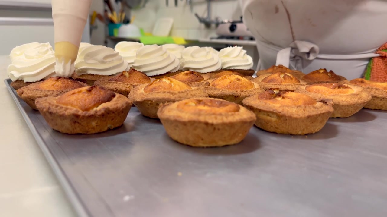 Primo piano medio di un pasticcere caucasico in sovrappeso che aggiunge crema con una sac à poche a torte appena preparate.
