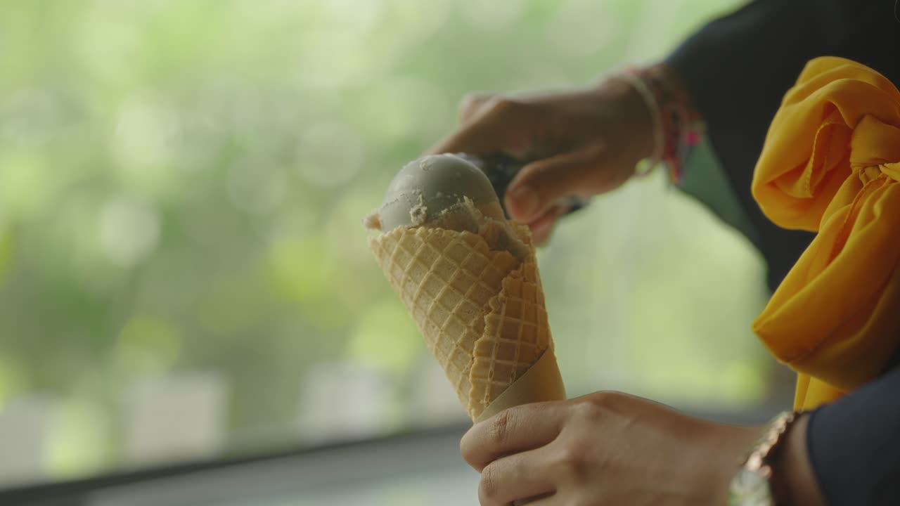manos sosteniendo un cono de pastelería sacando una bola de helado con una cuchara, de cerca