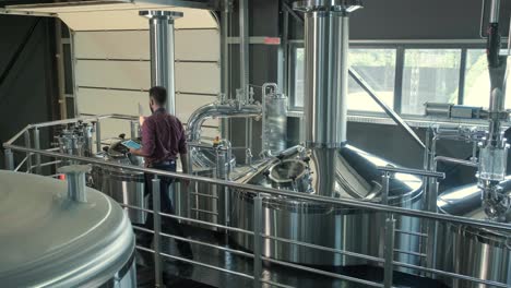 young male brewer wearing a leather apron supervise the process of beer fermentation at a modern brewery factory