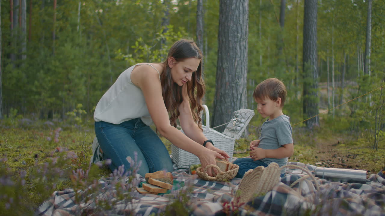 picnic familiar en el bosque madre joven y su pequeño hijo están sentados en una manta y preparando comida fin de semana en la naturaleza