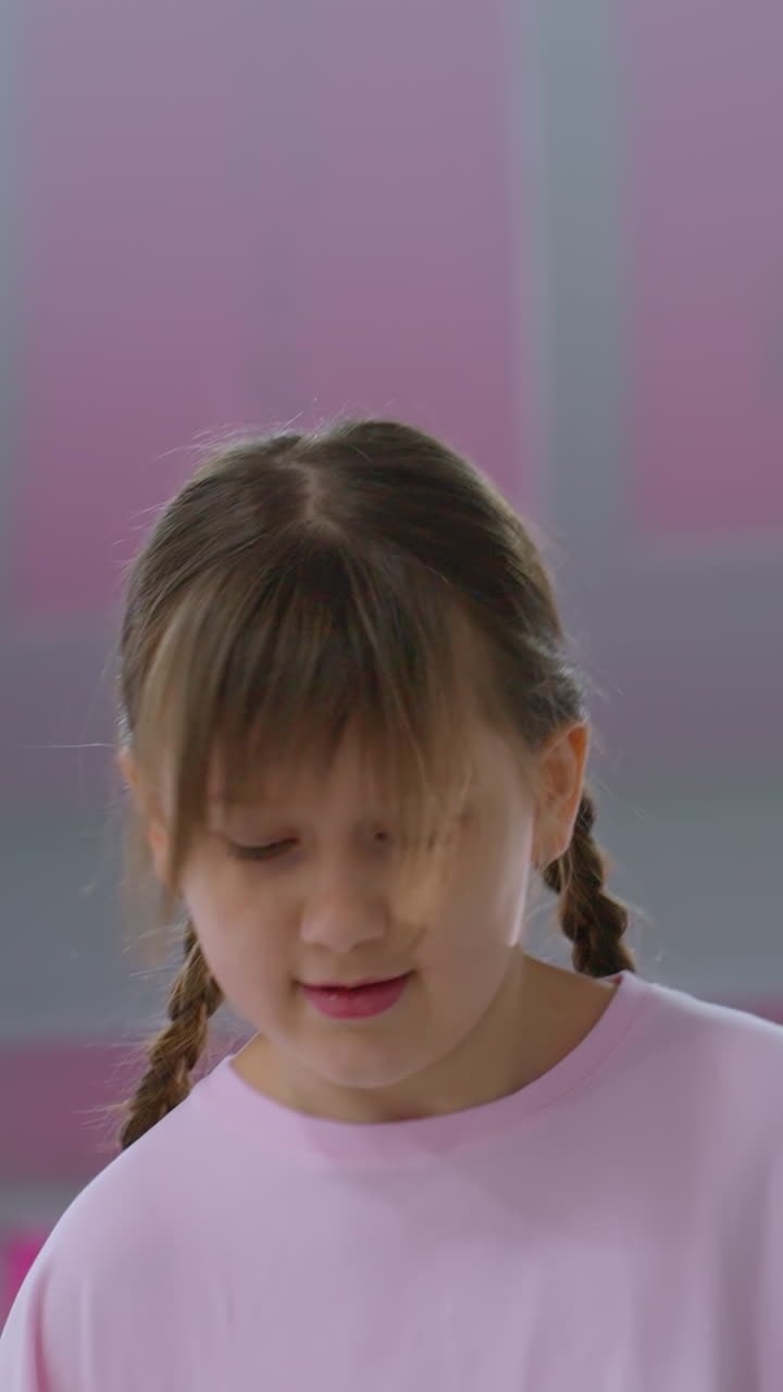 primer plano de una joven en salto medio rosa durante una sesión de entrenamiento, el cabello levantado por el movimiento, con un fondo borroso con el interior del gimnasio y luces brillantes del techo que se reflejan en los paneles de vidrio