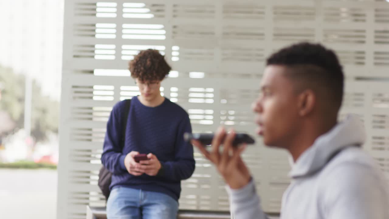 Uomo afroamericano che invia un messaggio dal telefono mentre aspetta alla fermata dell'autobus, scorrendo il telefono, con spazio per il testo.