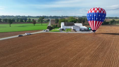 drone approaching shot of american hot air balloon on farm field near farm house and driving cars on road