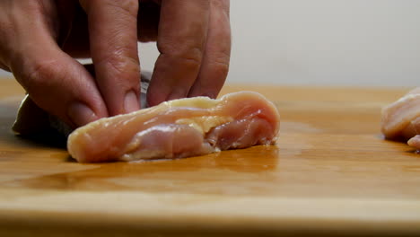 hand slices raw chicken into strips