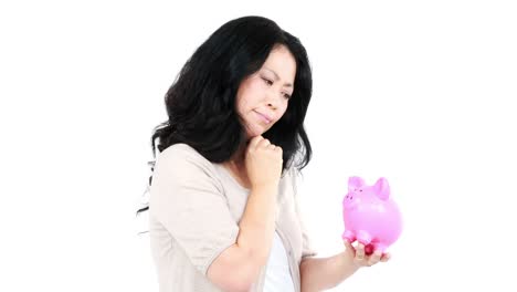 thoughtful asian woman holding and looking a piggy bank