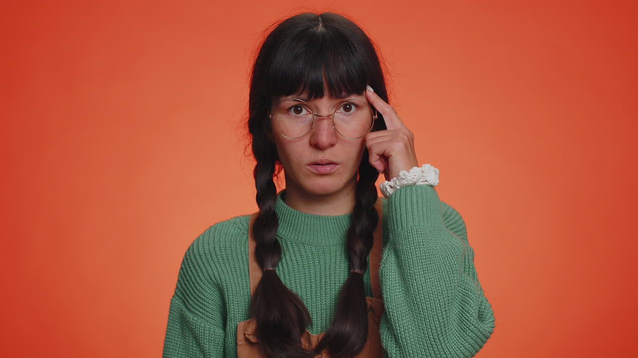 젊은 괴짜 여성이 카메라를 가리키고 어리석은 몸짓을 하며, 미친 짓을 한 바보를 비난합니다.