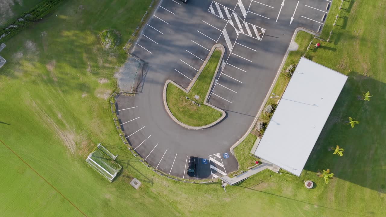 Drone footage captures a soccer field and adjacent carpark under bright daylight, showcasing the layout and surrounding greenery