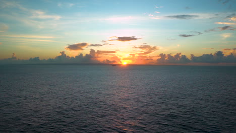 Espectacular-Vista-De-Lapso-De-Tiempo-Del-Sol-Saliendo-Desde-Más-Allá-Del-Horizonte-Caribeño,-Cielo-Azul-Arriba,-Nubes-Que-Se-Asemejan-Al-Horizonte-De-Una-Ciudad,-Un-Crucero-Distante-Que-Pasa-El-Disco-Solar,-Tiro-Panorámico-De-Lapso-De-Tiempo-Panorámico