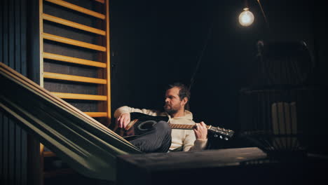 Musician-playing-his-guitar-unpretentiously-lying-on-hammock-at-home