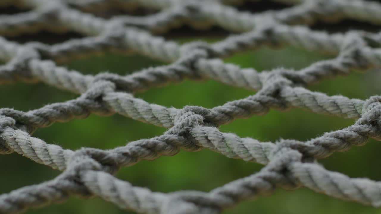 Close-up of a tightly knotted rope net outdoors with green blurred background