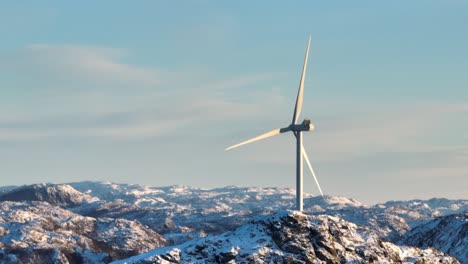 cinematic drone shot of windmills and spinning blades on top of mountain range on sunny winter day