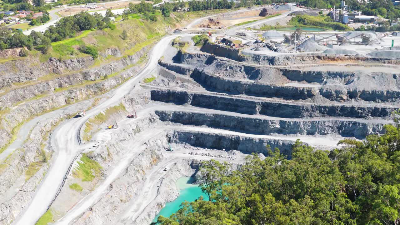Aerial footage of a tiered quarry in Gold Coast, Australia, showcasing mining activity under bright daylight