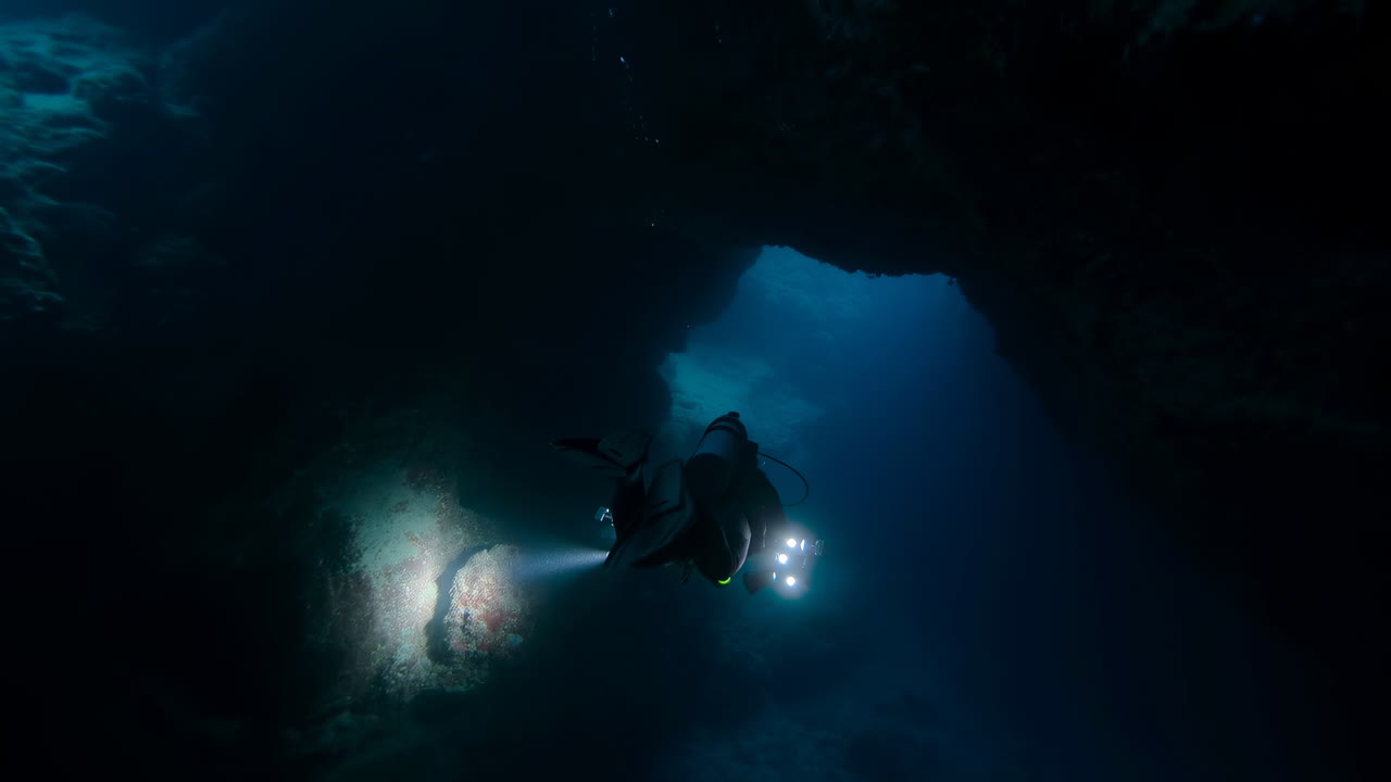 Diver With Torch Enters Underwater Cave Passage Revealing Blue Cavern Interior, Silhouette Gliding
