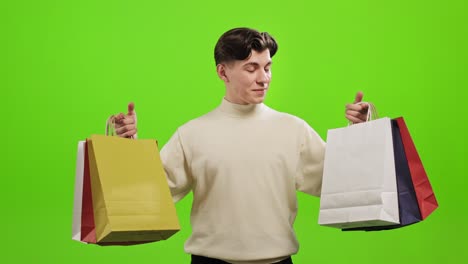un hombre sostiene bolsas de compras en ambas manos. las está mirando y levantando la cabeza. está sonriendo. está de pie sobre un fondo verde. pantalla verde. 4k.
