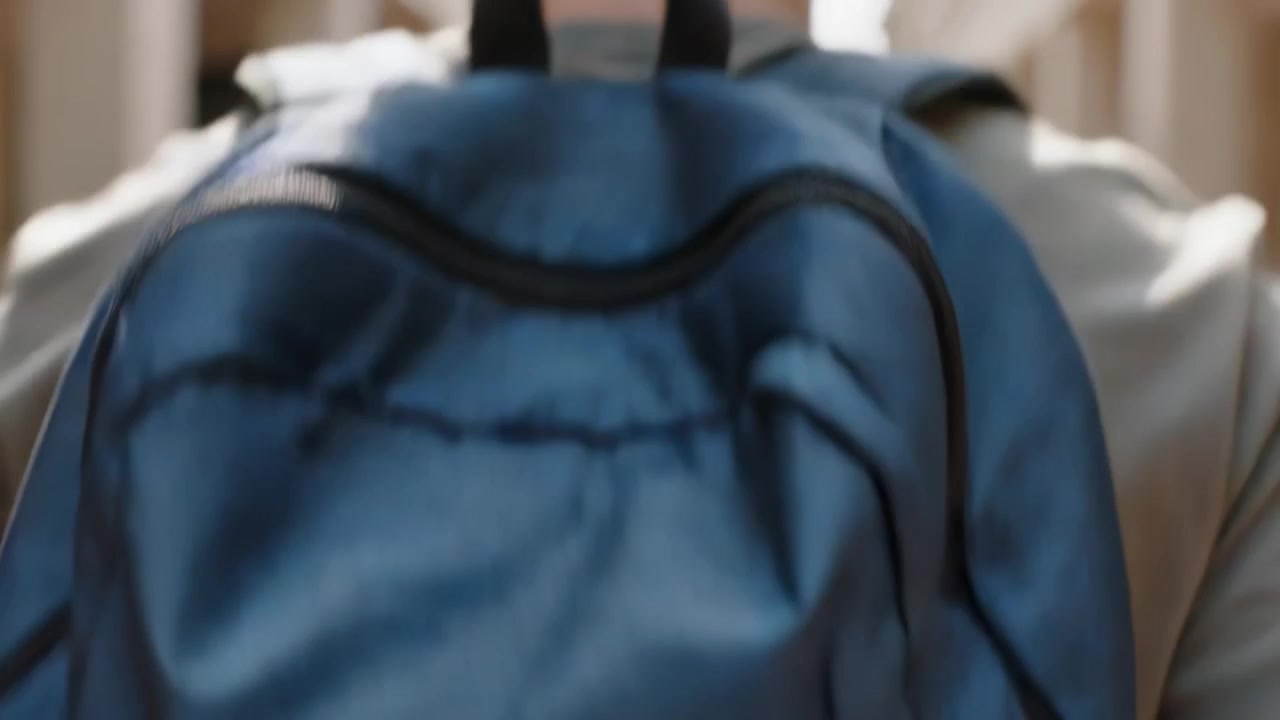 Walking student wearing light shirt with blue backpack down arcade after camera pull, heading exit
