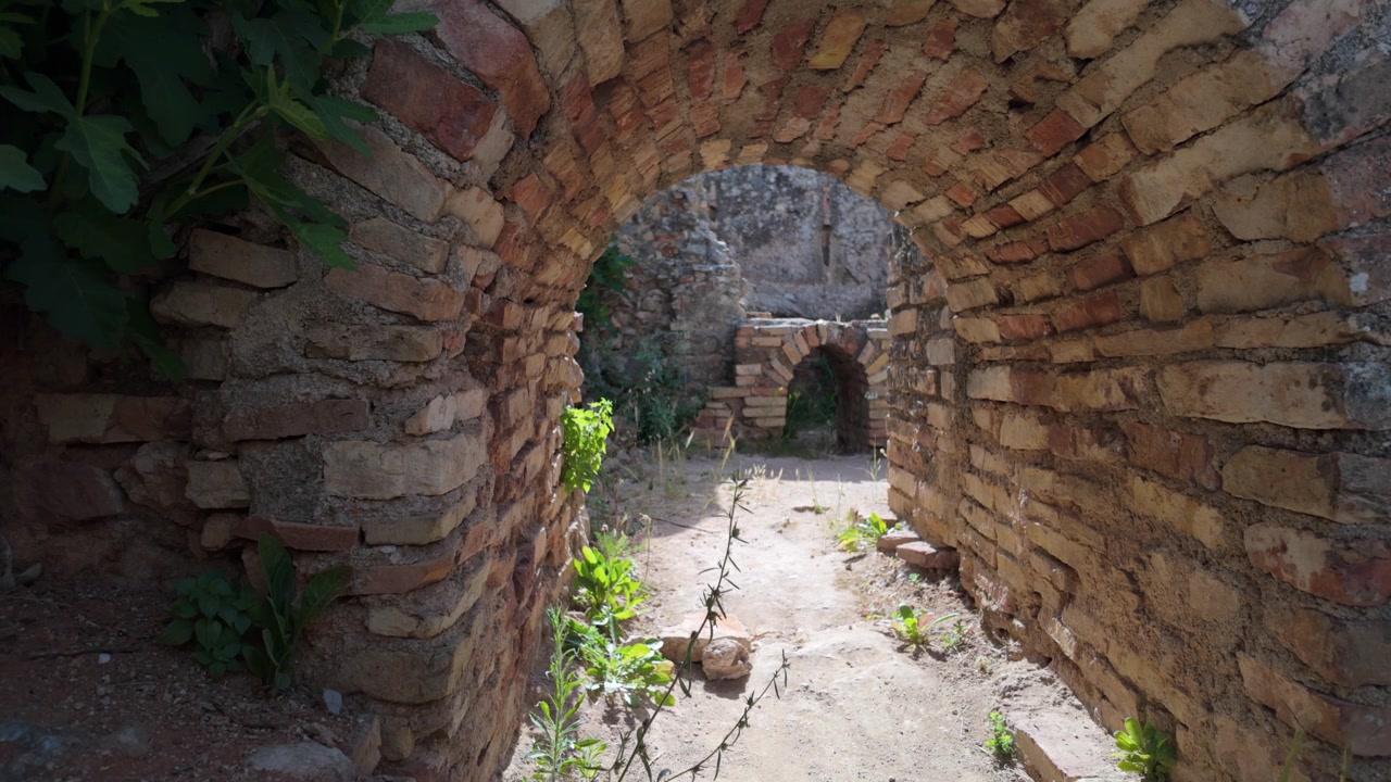 Vista a livello del suolo di un antico arco in mattoni all'interno del sito archeologico di Volubilis in Marocco, che mostra la muratura romana conservata e i resti architettonici storici.