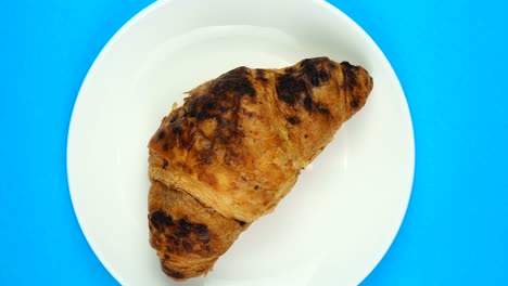 fresh croissant slow rotating on blue background. top view