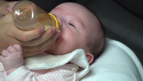 woman feeds her infant baby girl with formula milk from the bottle at home close up