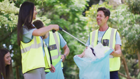 Diverse-group-of-male-and-female-friends-putting-plastic-rubbish-in-blue-refuse-sacks-in-forest