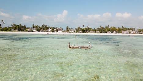 aerial view of a poor fisherman with a torn shirt sails on a small boat on clear blue water along a tropical beach with beautiful hotels in africa