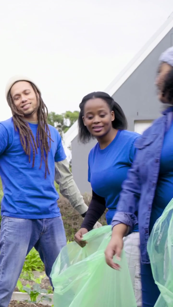 Vertical video: Holding green bag and talking, woman in blue shirt leading cleanup at garden