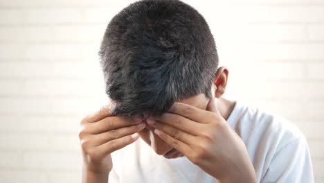 sad teenage boy covering his face sitting on sofa ,