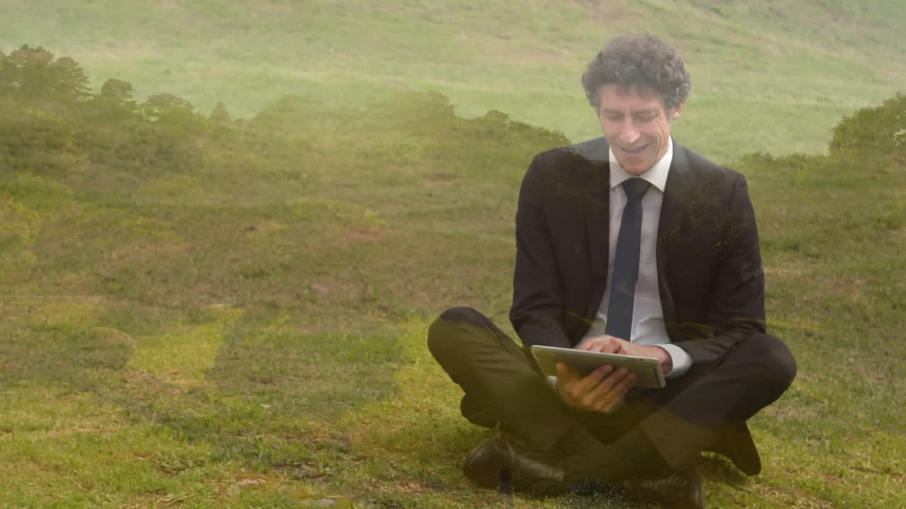 Businessman typing on his tablet while sitting on grass