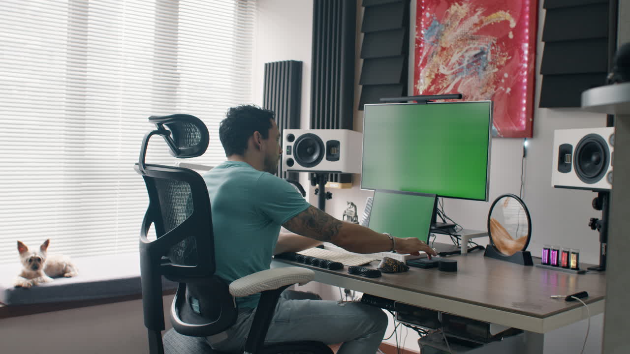 Man mixes audio on dual-screen setup in modern studio with green display