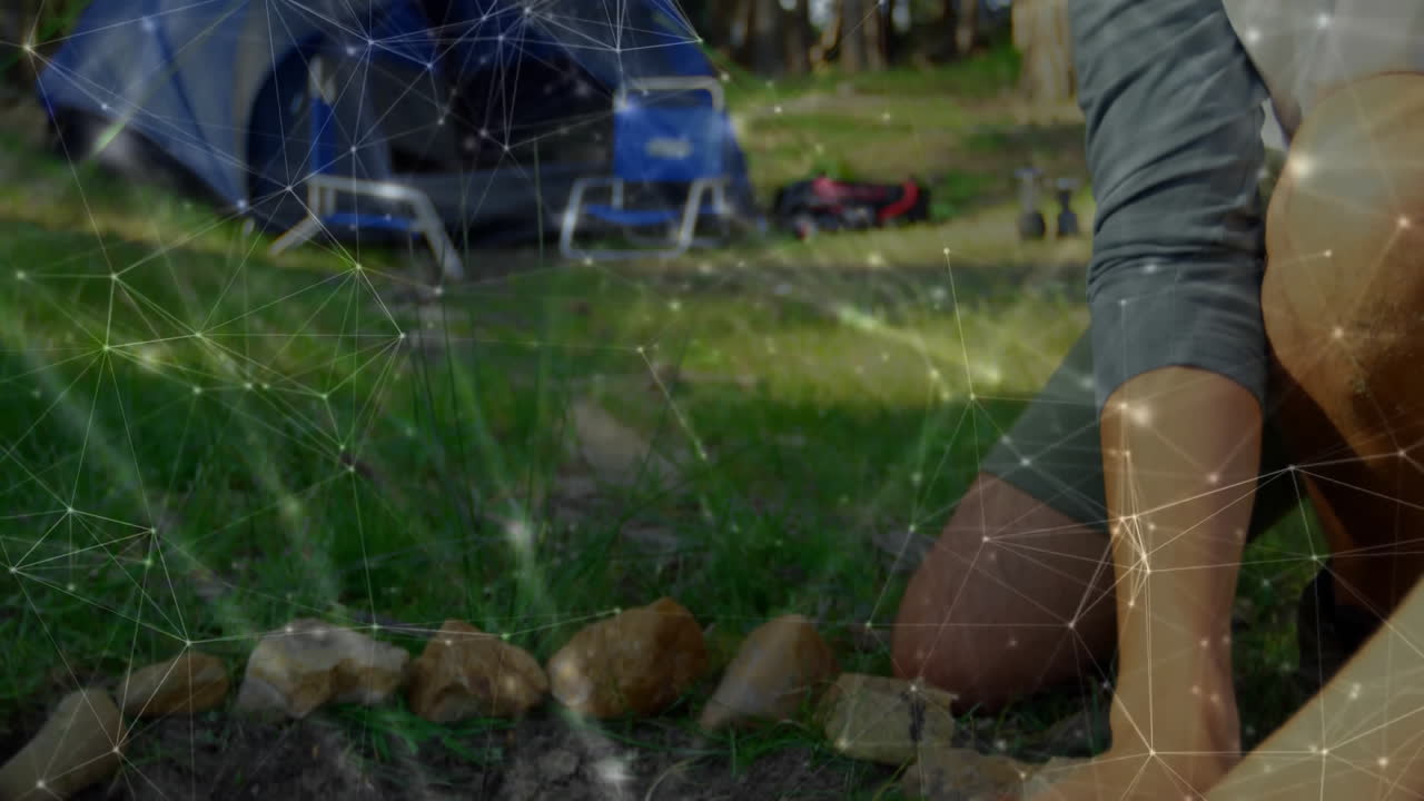 Marketing professional kneeling at forest campsite, analyzing network overlay connecting gear icons