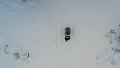 Vista-Aérea-De-Arriba-Hacia-Abajo-Del-Carro-De-Bebé-De-Empuje-Femenino-En-Una-Carretera-Nevada-Bajo-Los-árboles