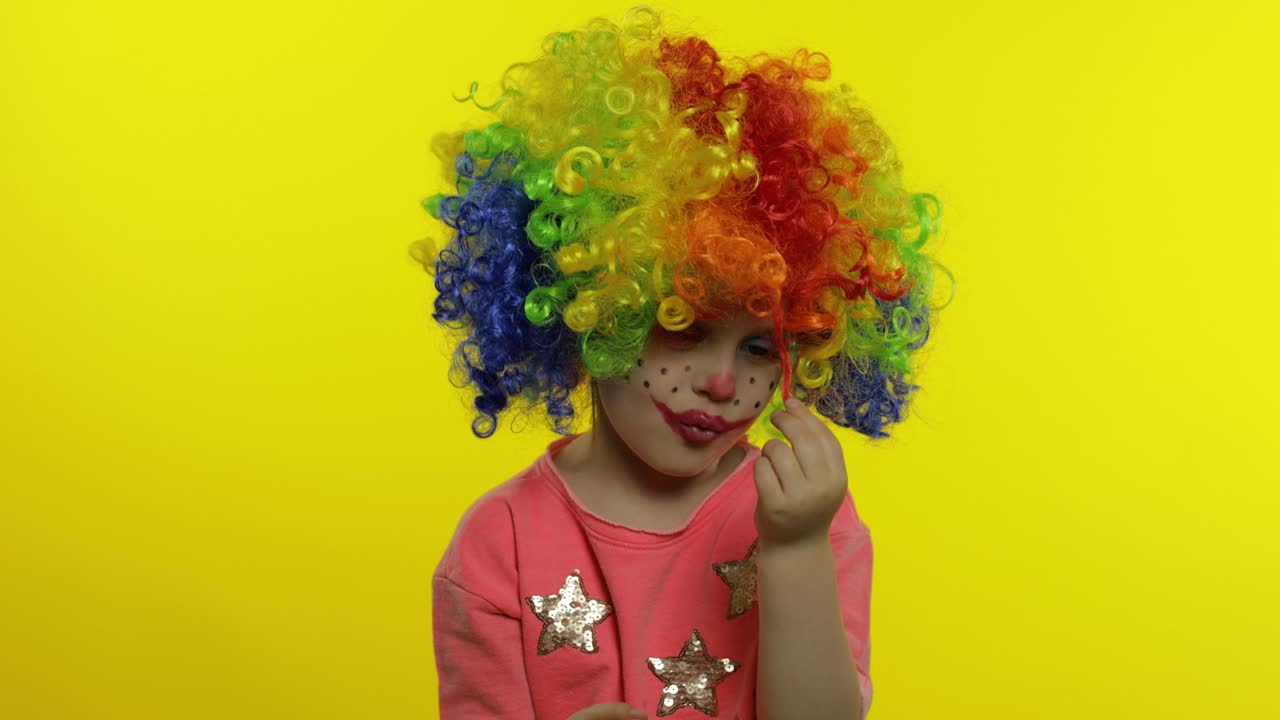 una niña payasa con una peluca arco iris haciendo caras tontas. tonto, sonriendo, bailando. halloween