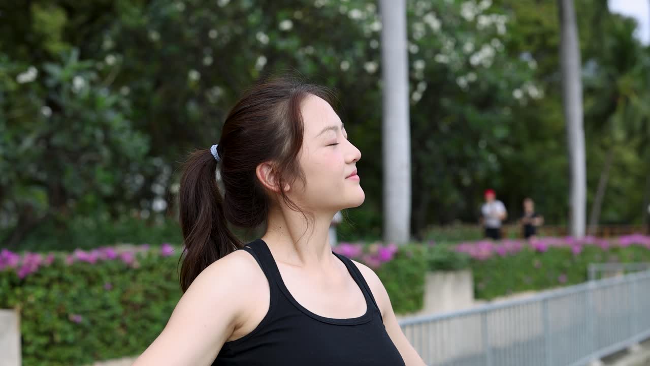 黒いスポーツウェアを着た女性が、晴れた公園で首を伸ばし、深呼吸をしています。