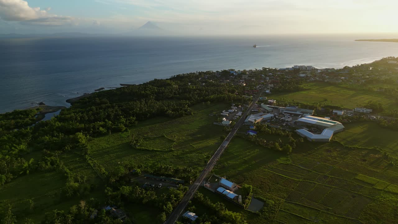 Panoramic aerial view of lush tropical island coastline, roads, and town during golden hour - San Andres, Catanduanes, Philippines