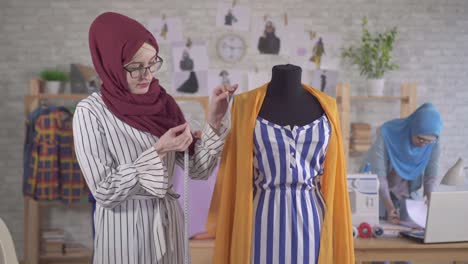 young muslim woman fashion designer in national headscarf takes measurements with a tape measure in a modern studio